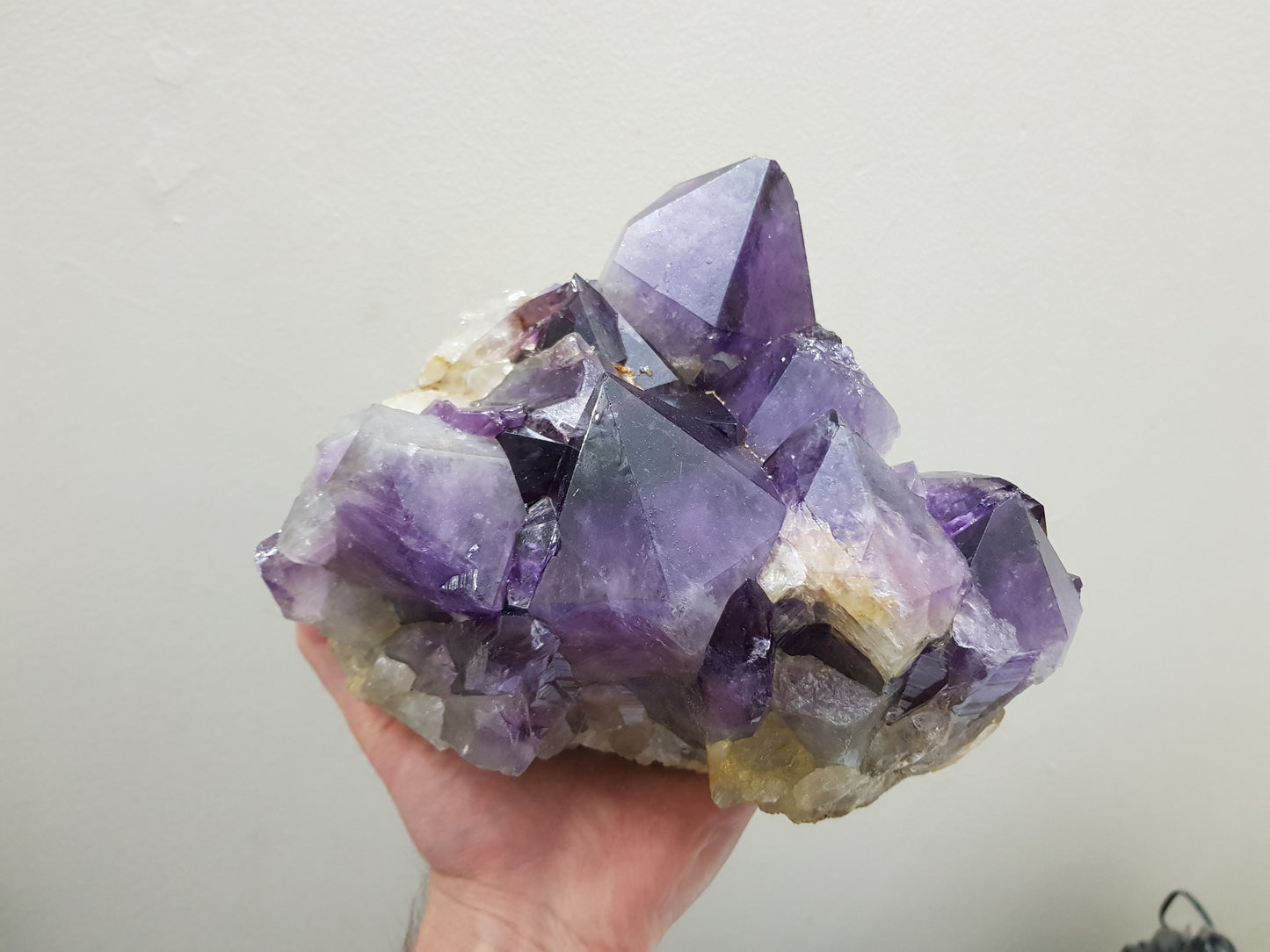 A hand holding an extra large natural amethyst crystal cluster that is approximately 17 centimetres by 16 centimetres in size