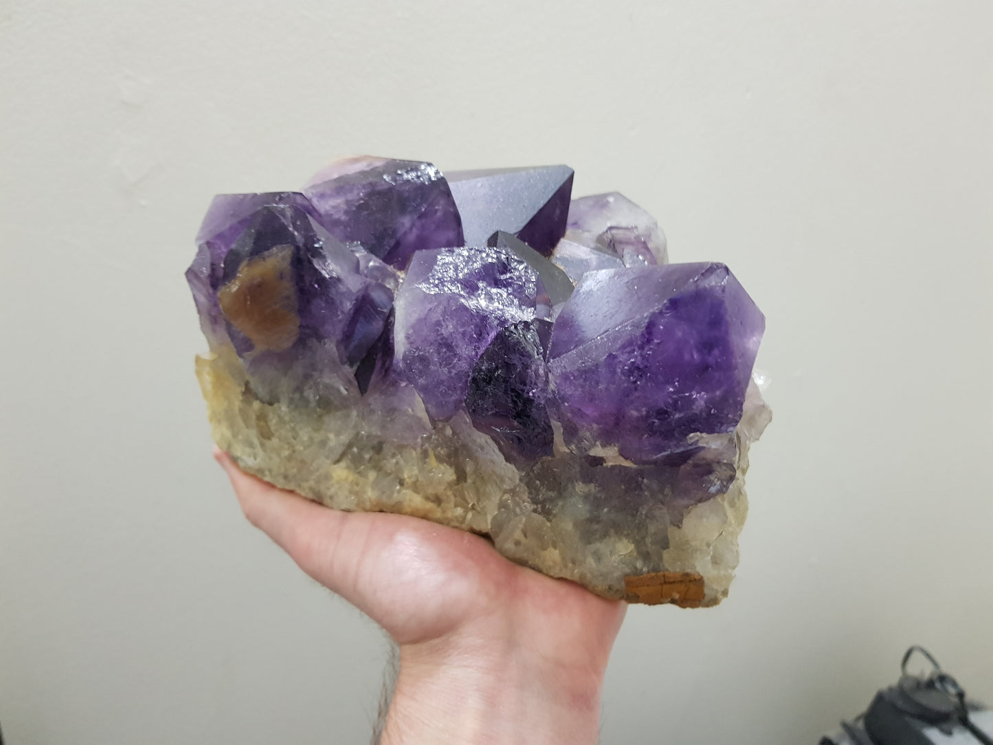 A hand holding an extra large natural amethyst crystal cluster that is approximately 17 centimetres by 16 centimetres in size