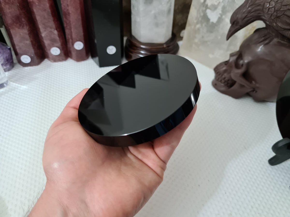 A hand holding a Black Obsidian crystal scrying mirror that is 10 centimetres in size