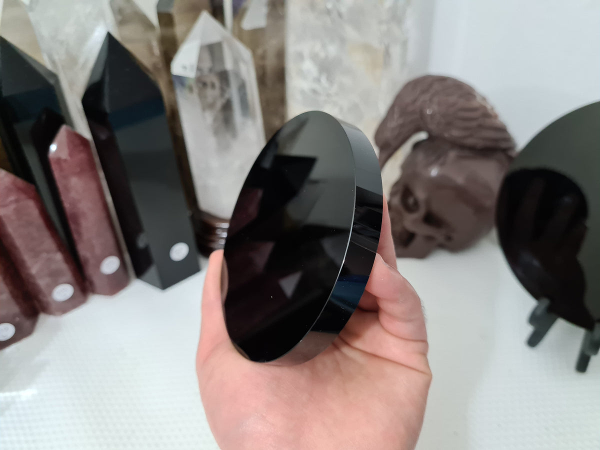 A hand holding a Black Obsidian crystal scrying mirror that is 10 centimetres in size