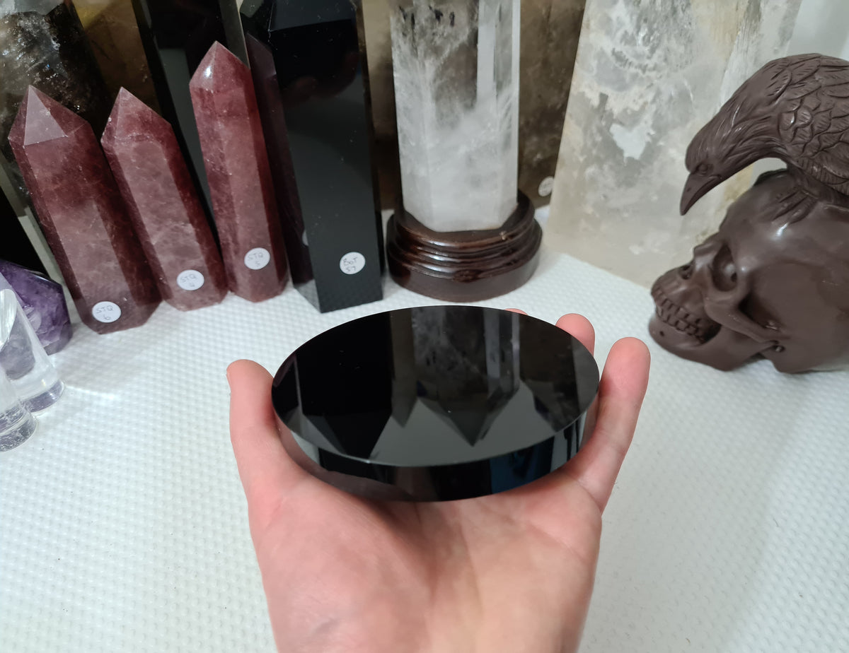 A hand holding a Black Obsidian crystal scrying mirror that is 10 centimetres in size