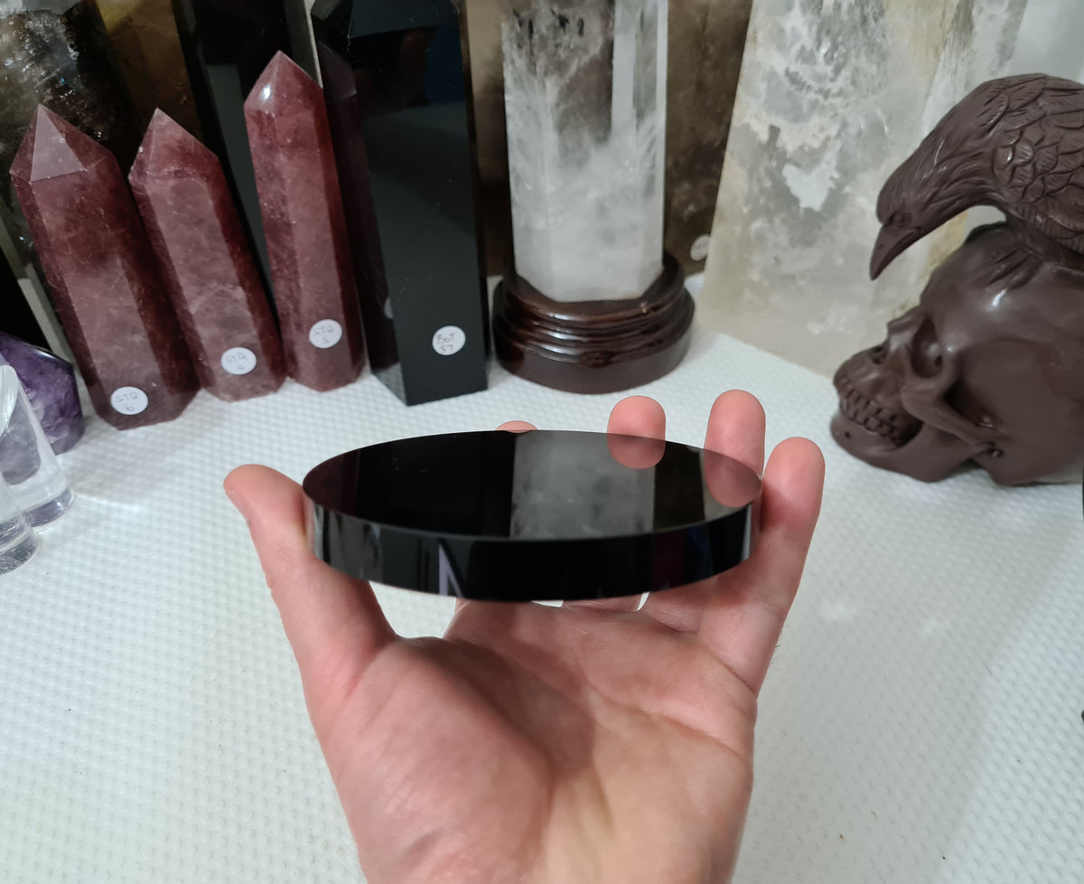 A hand holding a Black Obsidian crystal scrying mirror that is 10 centimetres in size