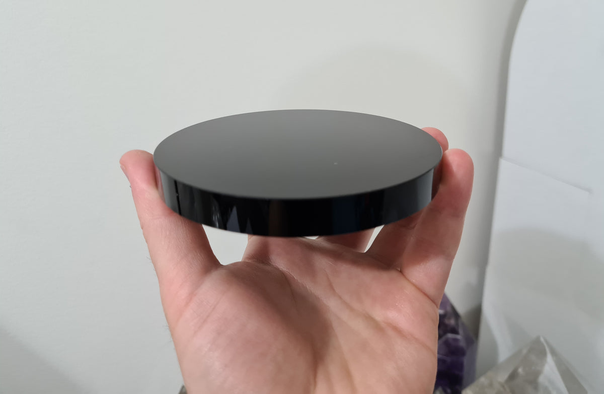 A hand holding a Black Obsidian crystal scrying mirror that is 10 centimetres in size