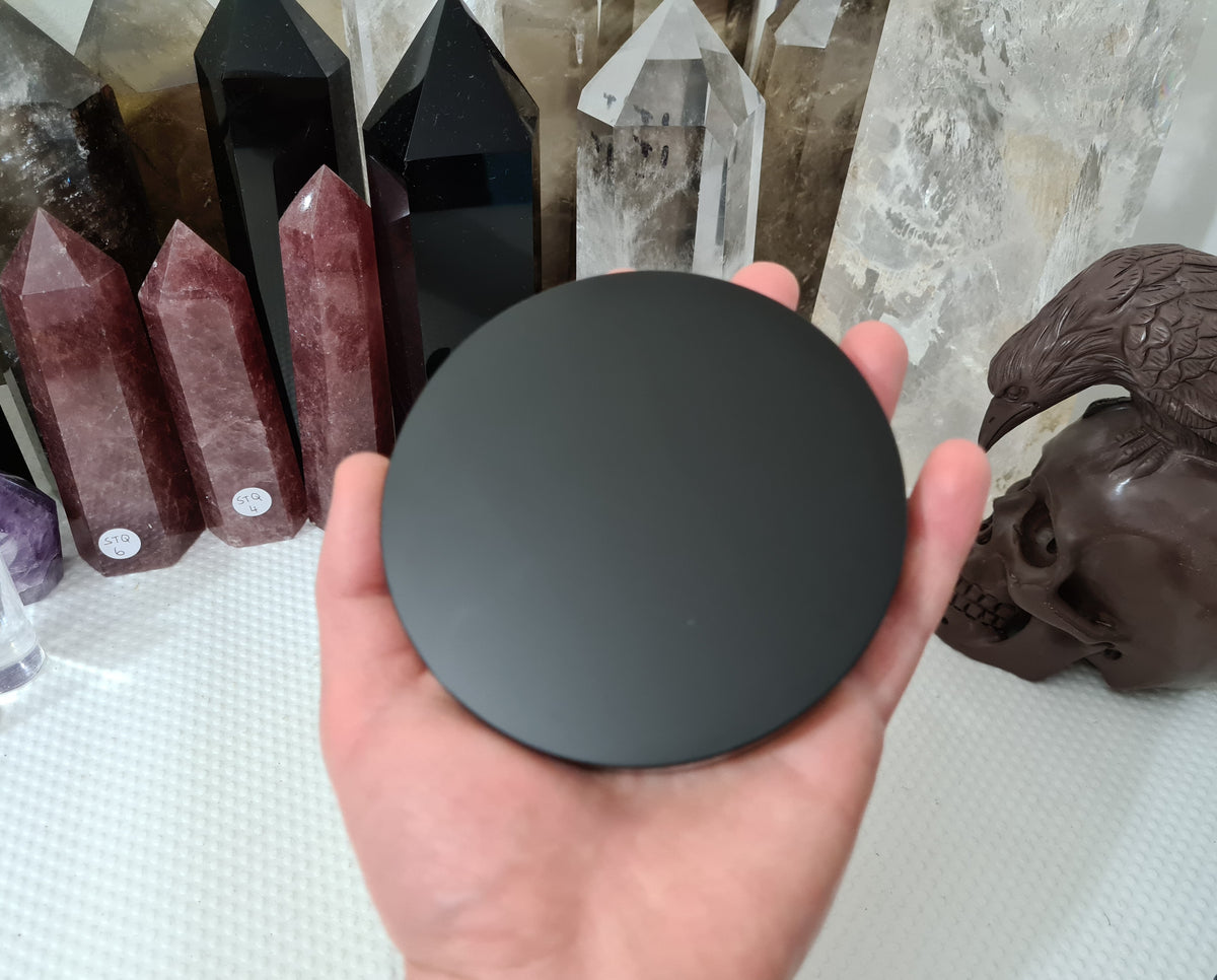 A hand holding a Black Obsidian crystal scrying mirror that is 10 centimetres in size
