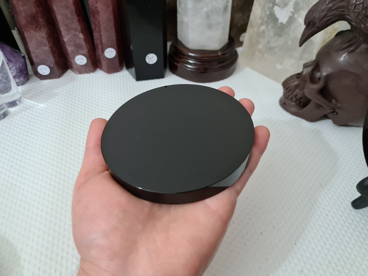 A hand holding a Black Obsidian crystal scrying mirror that is 10 centimetres in size