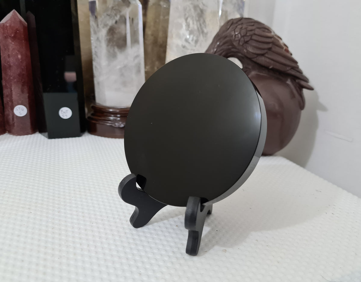 A Black Obsidian crystal scrying mirror that is 10 centimetres in size resting in a stand