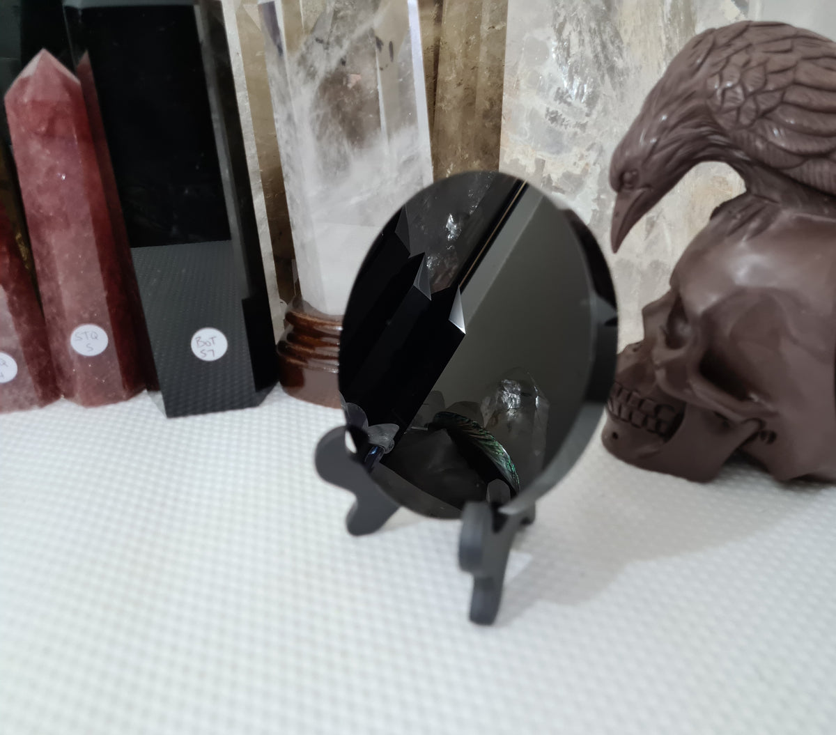 A Black Obsidian crystal scrying mirror that is 10 centimetres in size resting in a stand