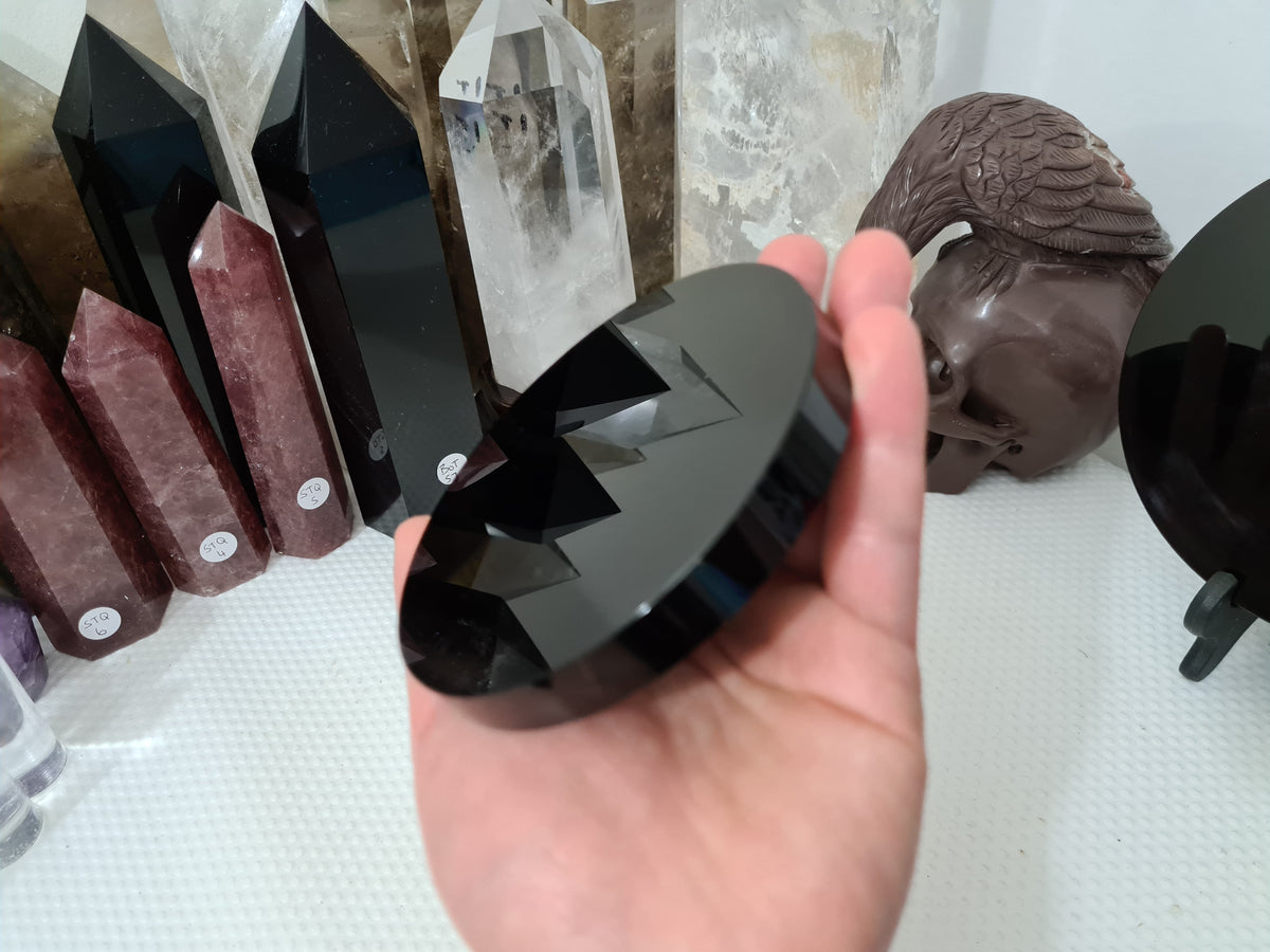 A hand holding a Black Obsidian crystal scrying mirror that is 10 centimetres in size