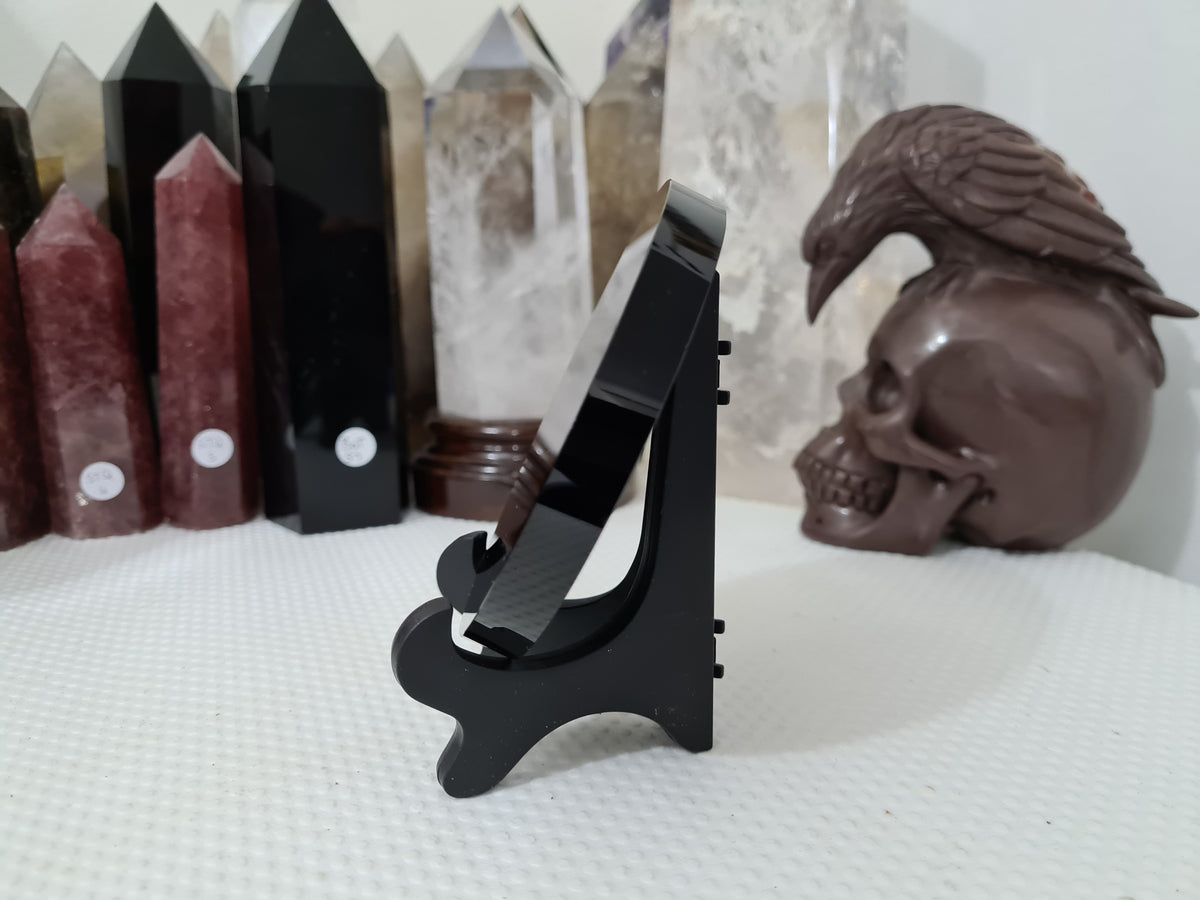 A Black Obsidian crystal scrying mirror that is 10 centimetres in size resting in a stand