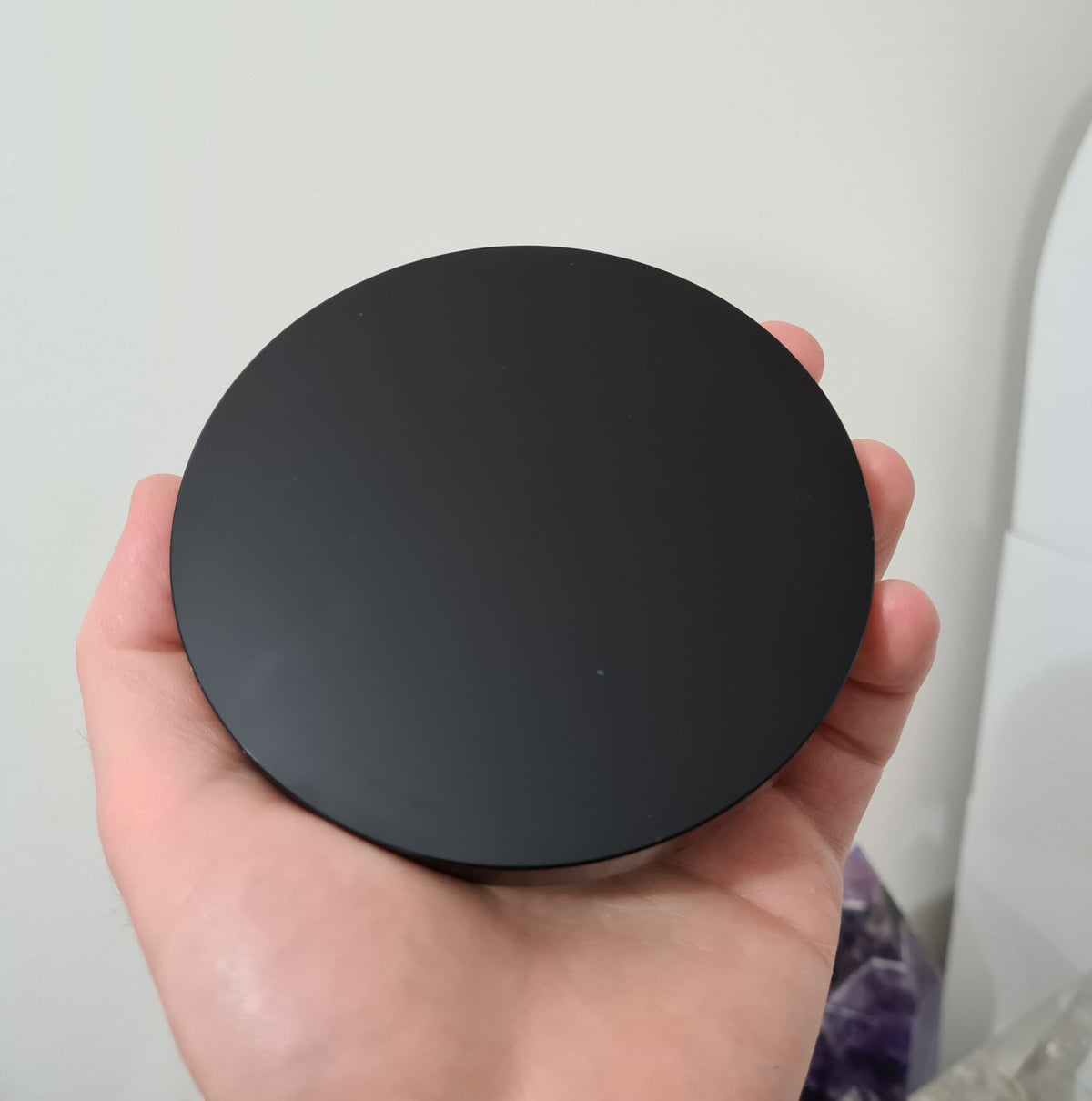A hand holding a Black Obsidian crystal scrying mirror that is 10 centimetres in size