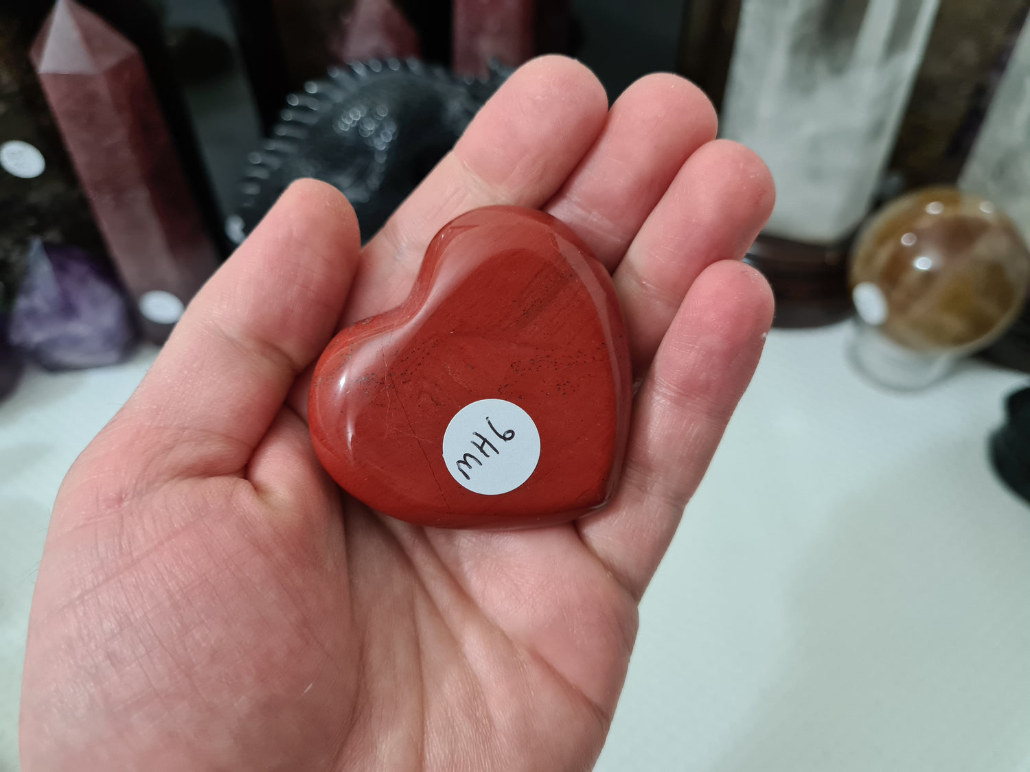 A hand holding a Mookaite crystal heart that is approximately 5 centimetres by 5 centimetres in size
