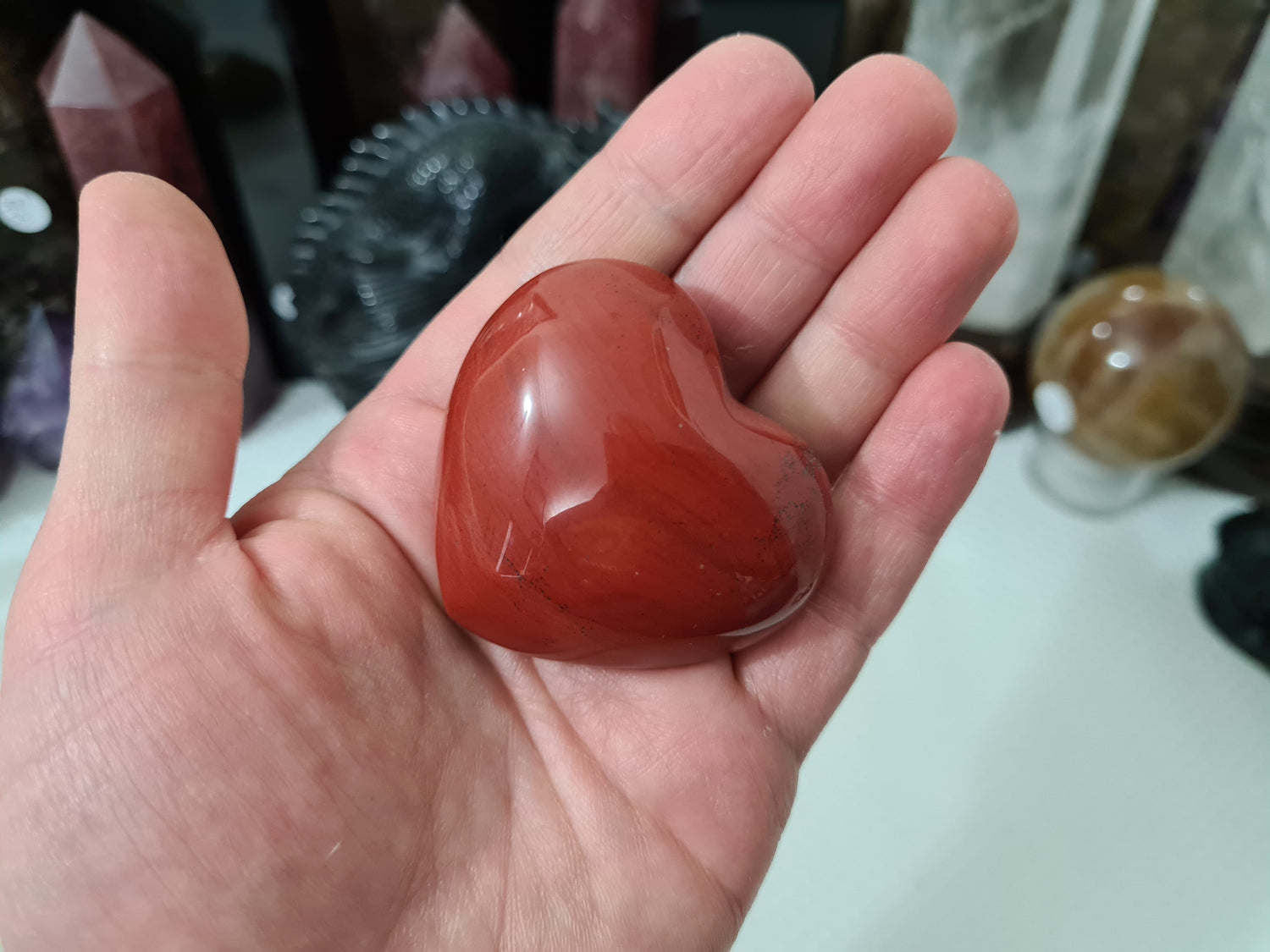 A hand holding a Mookaite crystal heart that is approximately 5 centimetres by 5 centimetres in size
