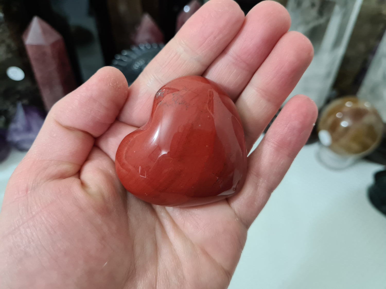 A hand holding a Mookaite crystal heart that is approximately 5 centimetres by 5 centimetres in size