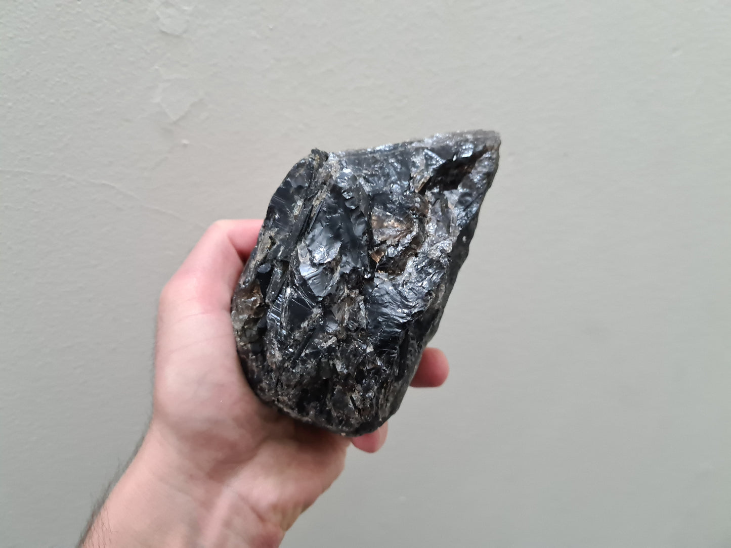 A hand holding a natural Smoky Quartz crystal chunk that is approximately 12.5 centimetres by 8.5 centimetres in size