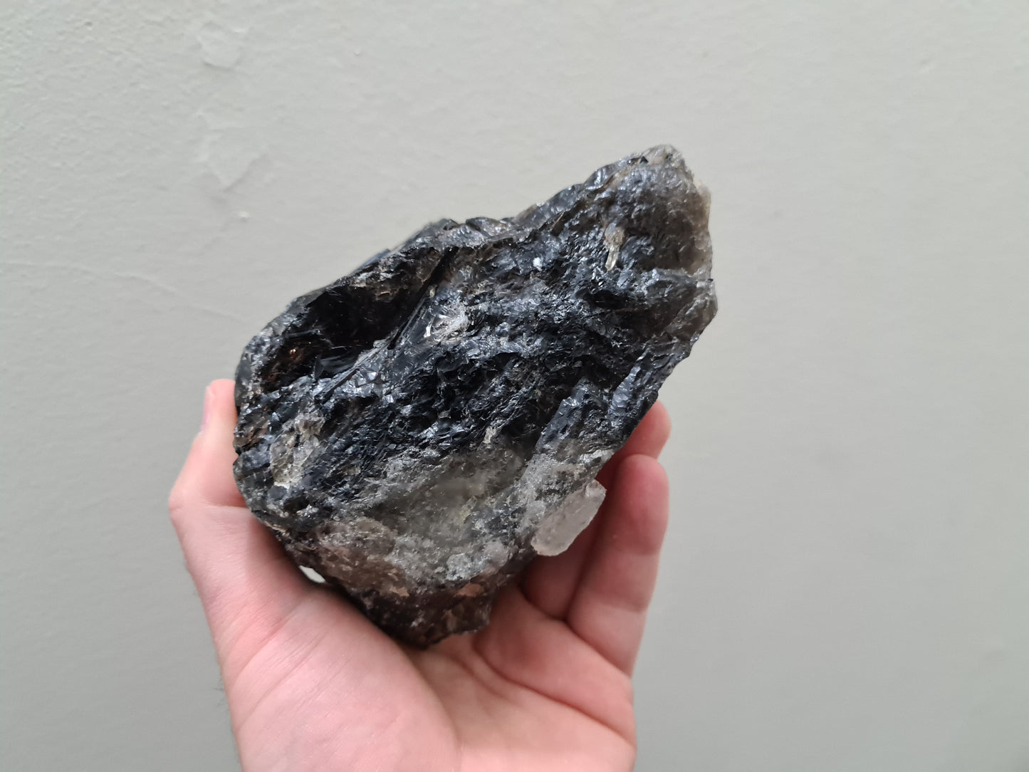 A hand holding a natural Smoky Quartz crystal chunk that is approximately 12.5 centimetres by 8.5 centimetres in size