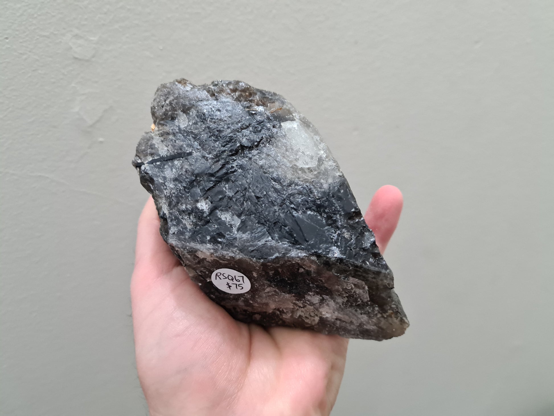 A hand holding a natural Smoky Quartz crystal chunk that is approximately 12.5 centimetres by 8.5 centimetres in size