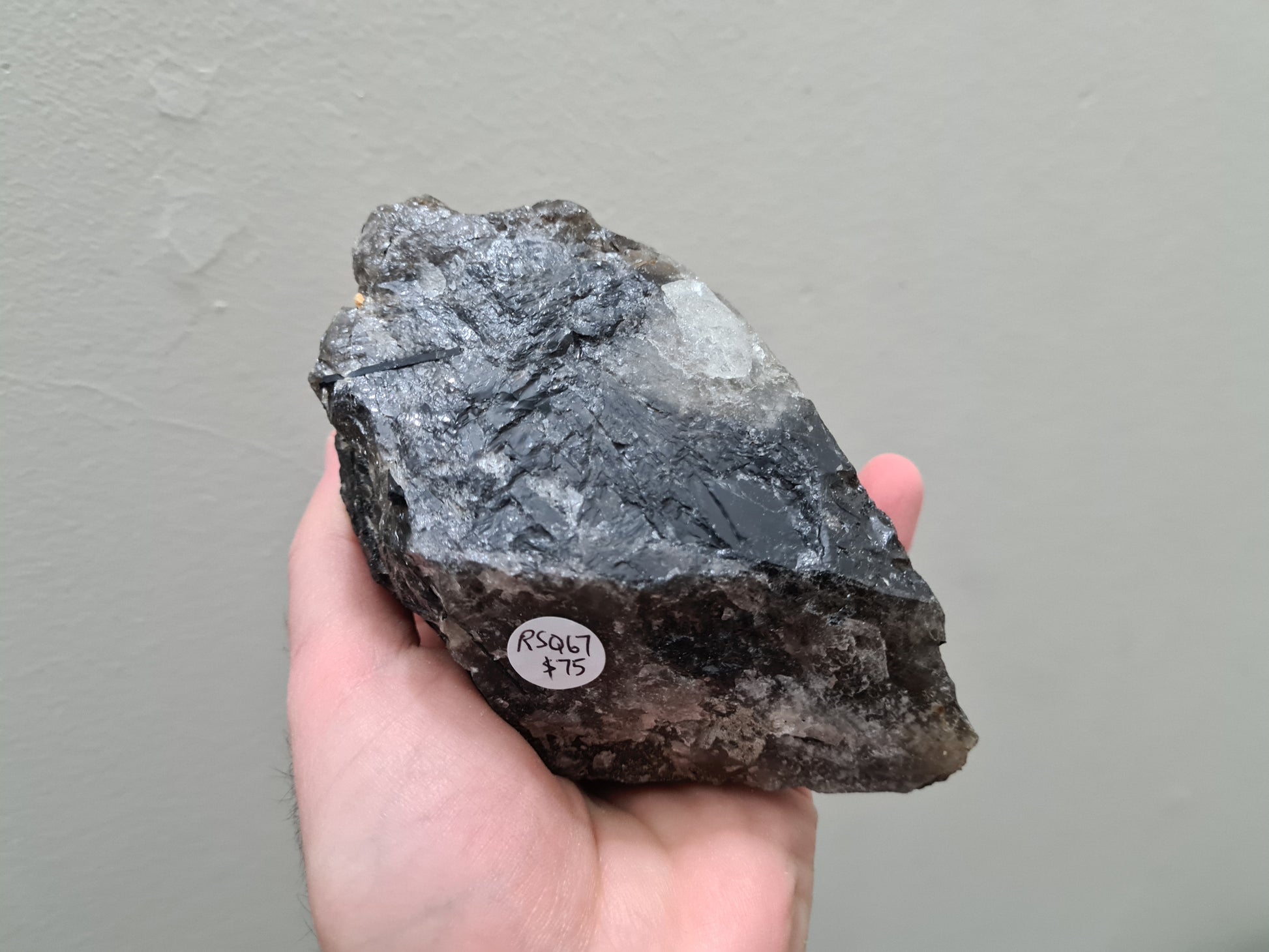 A hand holding a natural Smoky Quartz crystal chunk that is approximately 12.5 centimetres by 8.5 centimetres in size