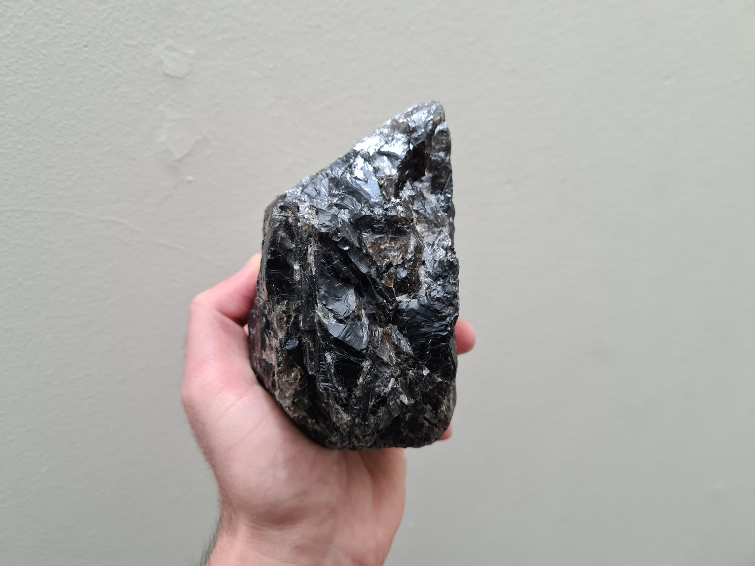 A hand holding a natural Smoky Quartz crystal chunk that is approximately 12.5 centimetres by 8.5 centimetres in size