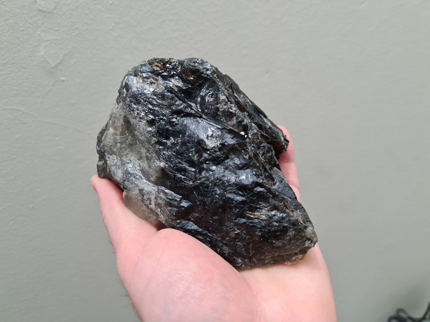A hand holding a natural Smoky Quartz crystal chunk that is approximately 12.5 centimetres by 8.5 centimetres in size