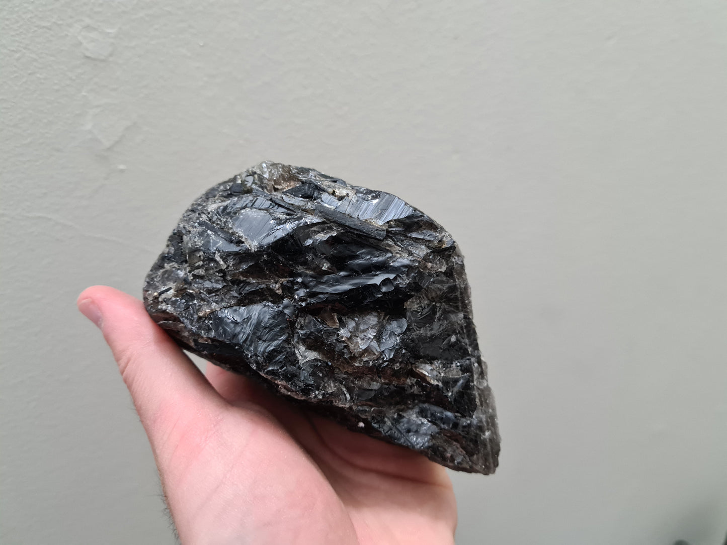 A hand holding a natural Smoky Quartz crystal chunk that is approximately 12.5 centimetres by 8.5 centimetres in size